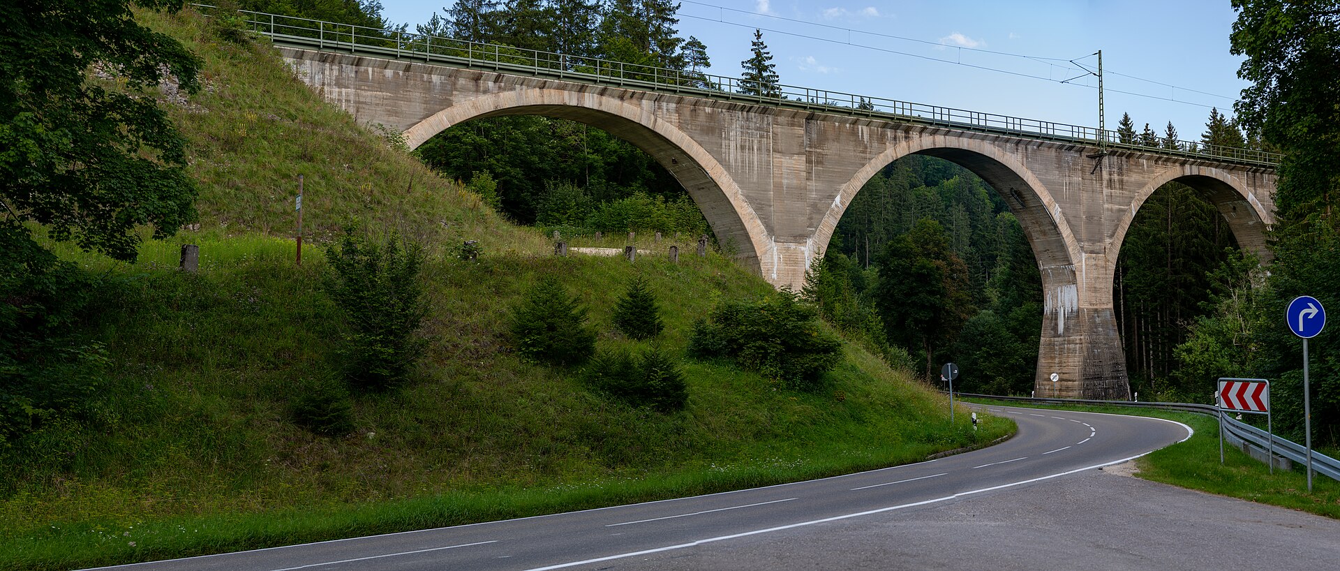 Ein Zug der Schwarzwaldbahn fährt über ein steinernes Viadukt zwischen bewaldeten Hängen.